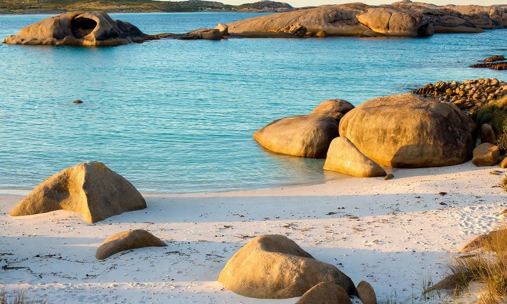 Smooth granite boulders on the white sand of Twilight Beach with calm turquoise water, Esperance