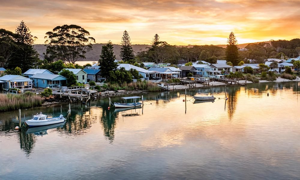 Sunset over the calm water at Huskisson with boats moored and trees along the shore