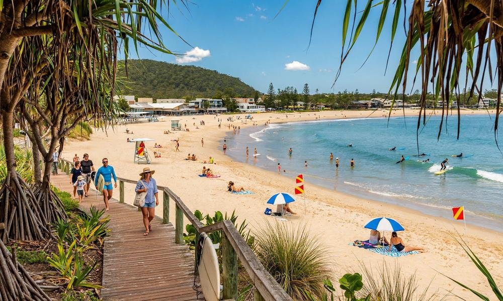 Noosa Main Beach with calm waves, pandanus trees and swimmers on the Sunshine Coast