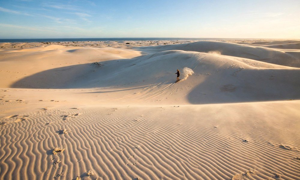 Sandboarder descending a tall sand ridge on the Stockton Sand Dunes