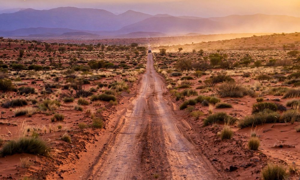 Red dirt road of the Red Centre Way running toward distant ranges in central Australia