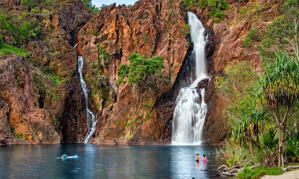 Wangi Falls cascading into a large calm swimming hole with swimmers in Litchfield National Park